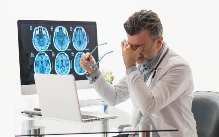 Stressed doctor rubbing eyes in front of computer screen, x-rays in the background