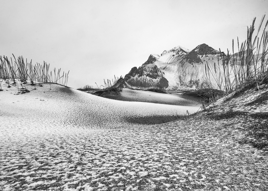 Black and white photo of dunes covered in snow with mountains in background in Iceland by Christopher B. Merritt, MD, FACR